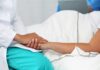 Healthcare worker holding a patient's hand in a hospital bed