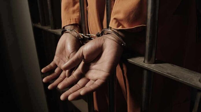 Prisoner in handcuffs behind jail bars